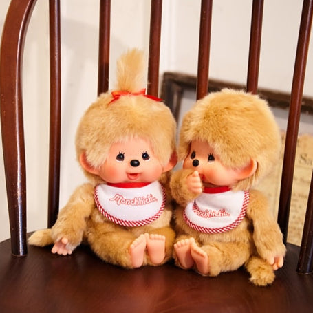 Two plush toys sitting on a wooden chair with a neutral background. Monchhichi